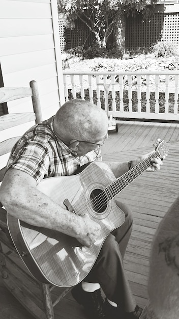 A black and white photo of a weathered Mississippi Delta shack with a musician sitting on the porch playing a blues guitar. A dust road is in front of the shack.