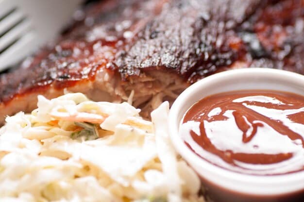 Close-up shot of a plate of Carolina-style pulled pork barbecue, showing the smoky meat, tangy vinegar sauce, and a side of coleslaw.