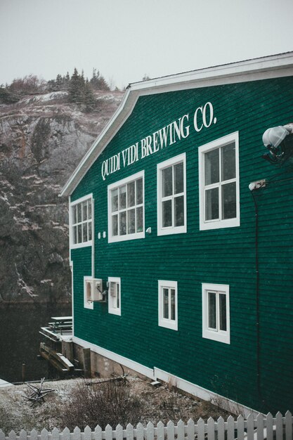 The exterior of a modern craft brewery located in a scenic mountain setting, with outdoor picnic tables, lush greenery, and a backdrop of snow-capped peaks, showcasing the brewery's integration with nature.