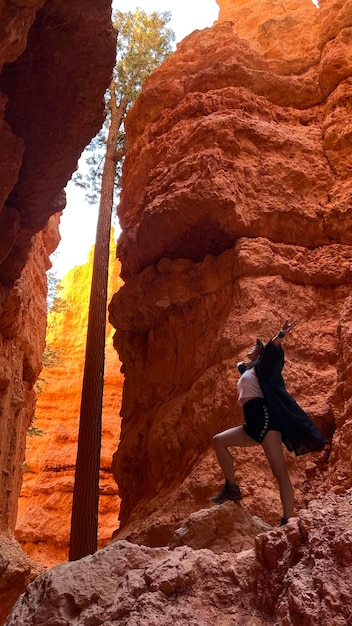 A rock climber ascending a sandstone cliff in Eldorado Canyon State Park, with the canyon's distinctive rock formations and lush vegetation visible in the background.