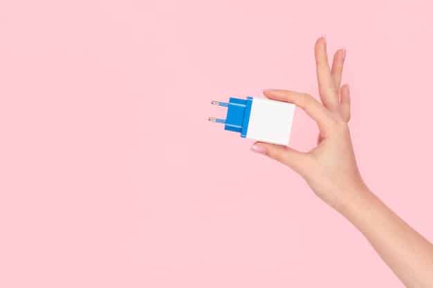 A hand holding a universal travel adapter, plugged into a foreign power outlet, with various plug types visible.