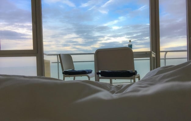 Interior view of a luxury cruise ship cabin, showcasing a balcony with ocean views, a comfortable bed, and modern amenities. The scene emphasizes comfort and relaxation.