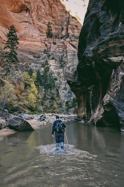 A captivating shot of a hiker navigating The Narrows in Zion National Park, wading through the Virgin River within the towering canyon walls. The image captures the adventurous spirit of an Unforgettable US Summer Vacation: A 12-Day National Parks Itinerary.