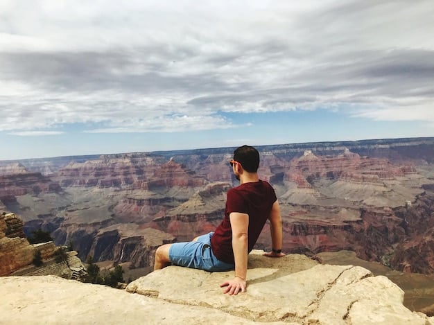 A photograph showing a solo hiker sitting on the edge of the Grand Canyon, taking a break and enjoying the spectacular view. The vastness of the canyon and the hiker's solitude create a sense of peace and adventure.