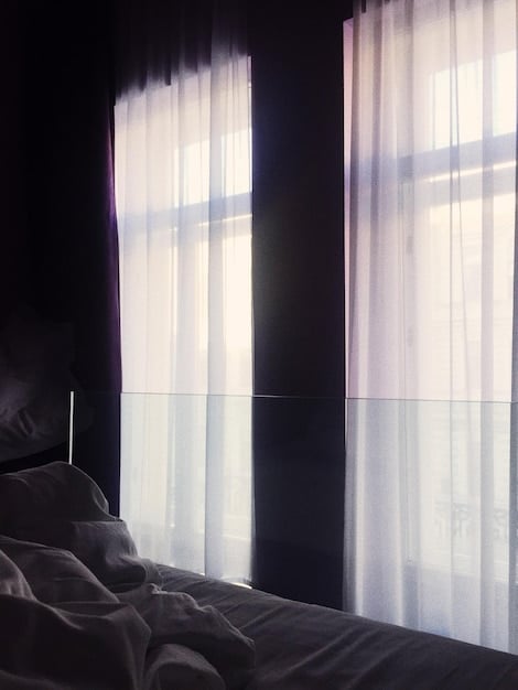 A dimly lit bedroom with comfortable bedding, blackout curtains, and a white noise machine on the nightstand, illustrating an optimized sleep environment to 'Beat Jet Lag: Adjust Your Sleep Schedule 3 Days Before You Fly'.