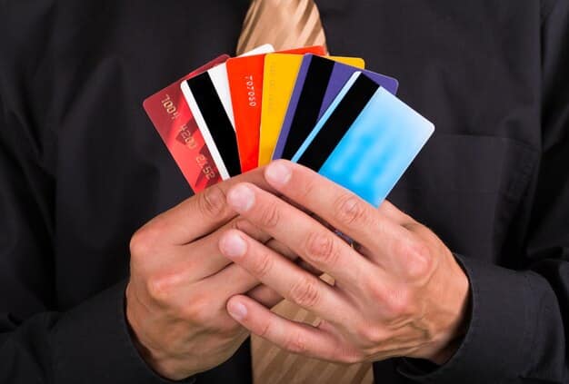 A hand holding multiple credit cards, fanned out to display their logos. The background is a blurred image of an airport terminal, suggesting the connection between credit card rewards and travel. The image emphasizes the strategic use of credit cards in travel hacking.